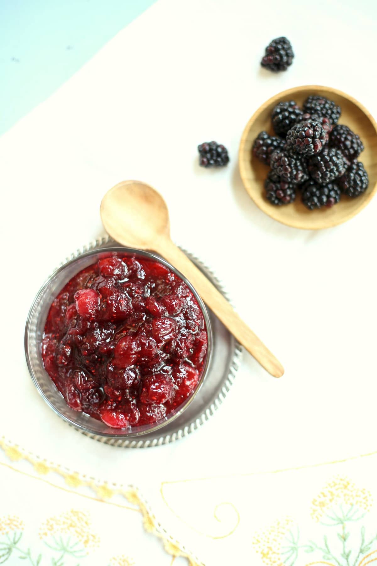 cranberry sauce in a silver and black dish, and fresh blackberries in a small wooden bowl on a table. 