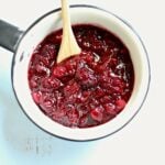 cranberry sauce in a white saucepan with a wodden spoon coming out the top side.