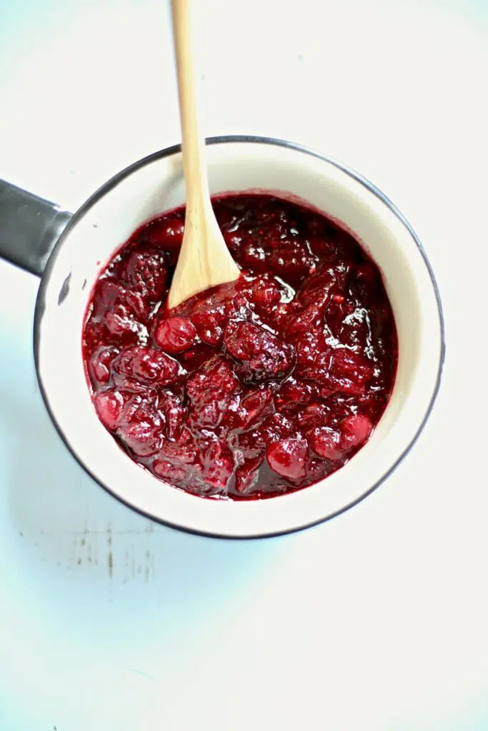cranberry sauce in a white saucepan with a wodden spoon coming out the top side.