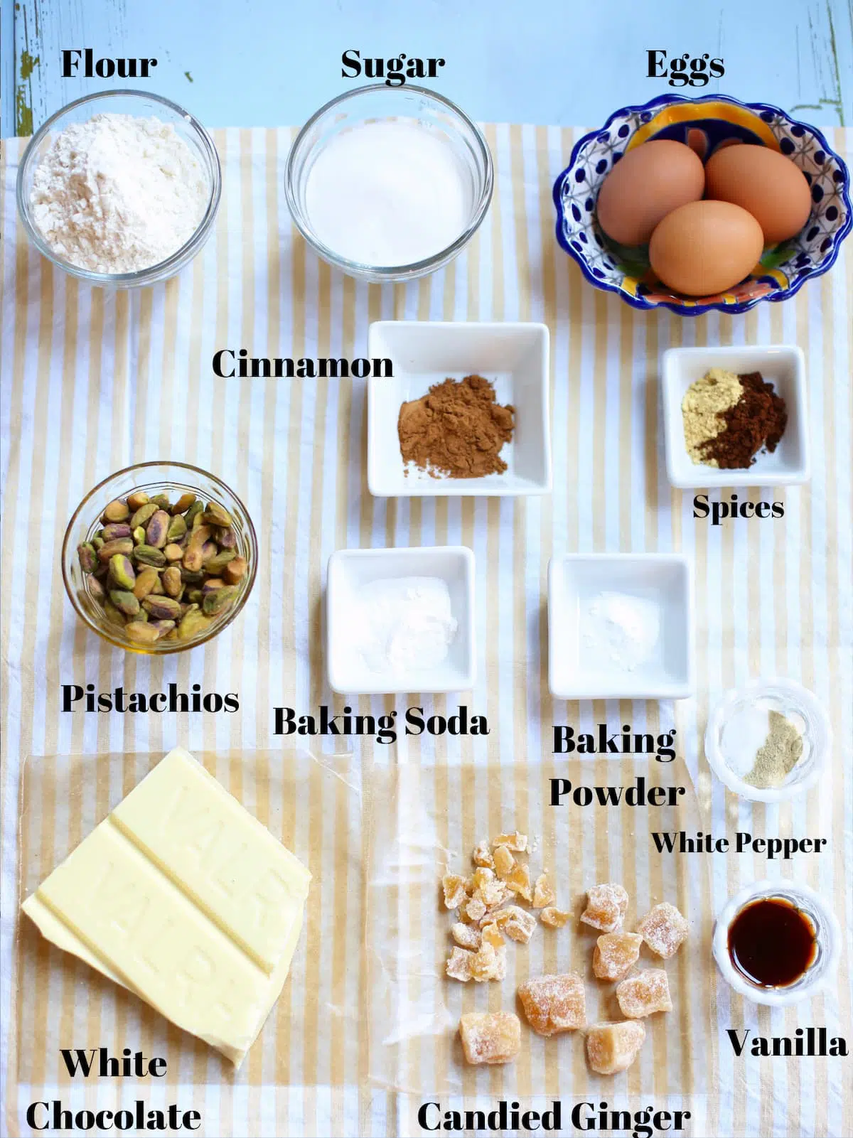 a table of ingredients for cookies, pisachios, white chocolate, cinnamon, spices, baking powder, bakig soda and vanilla.