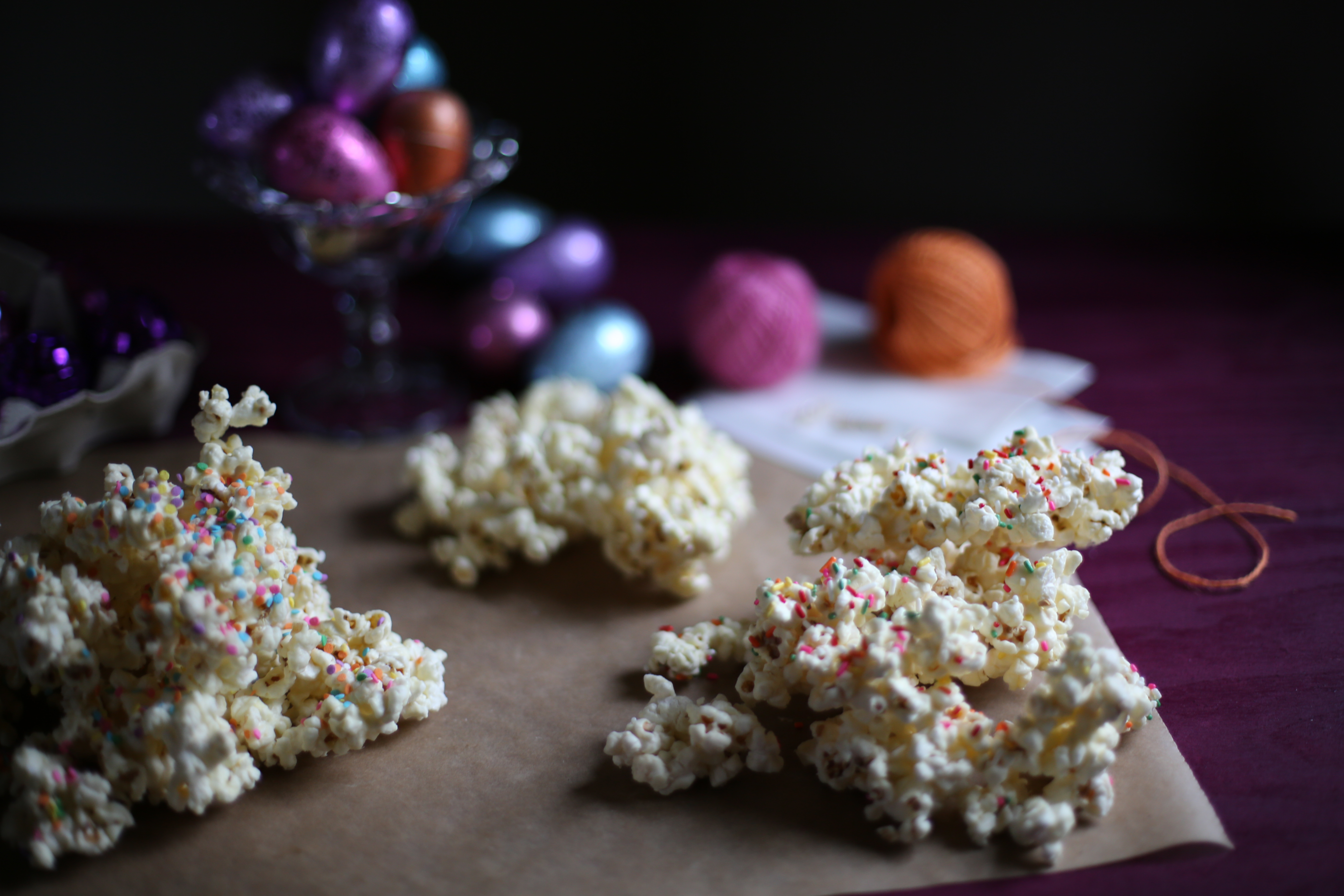 popcorn with sprinkles on a piece of parchment paper wih string and colored eggs behind 