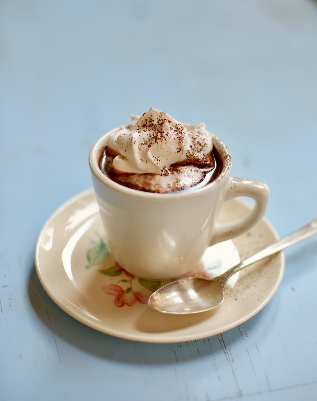 hot chocolate in a white cup with a silver spoon on a blue table 