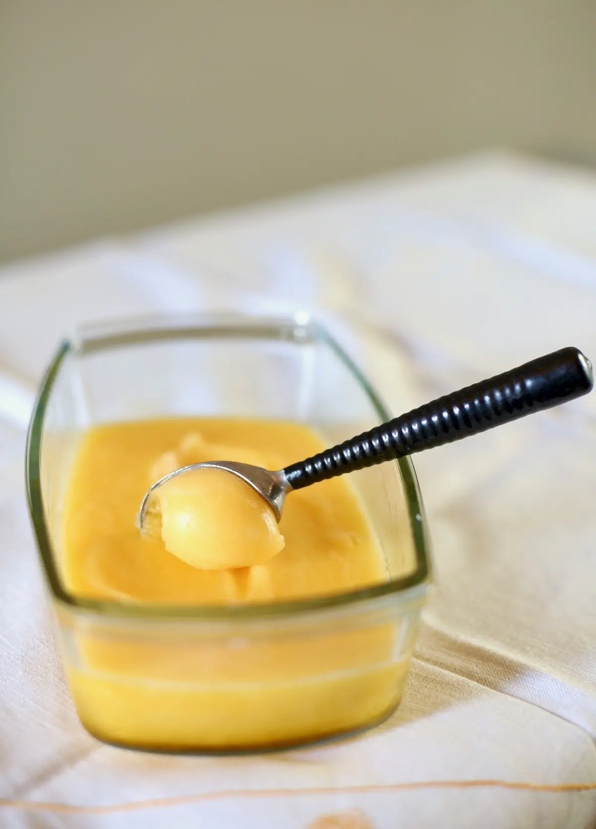 tangerine sorbet in a glass container with a scoop