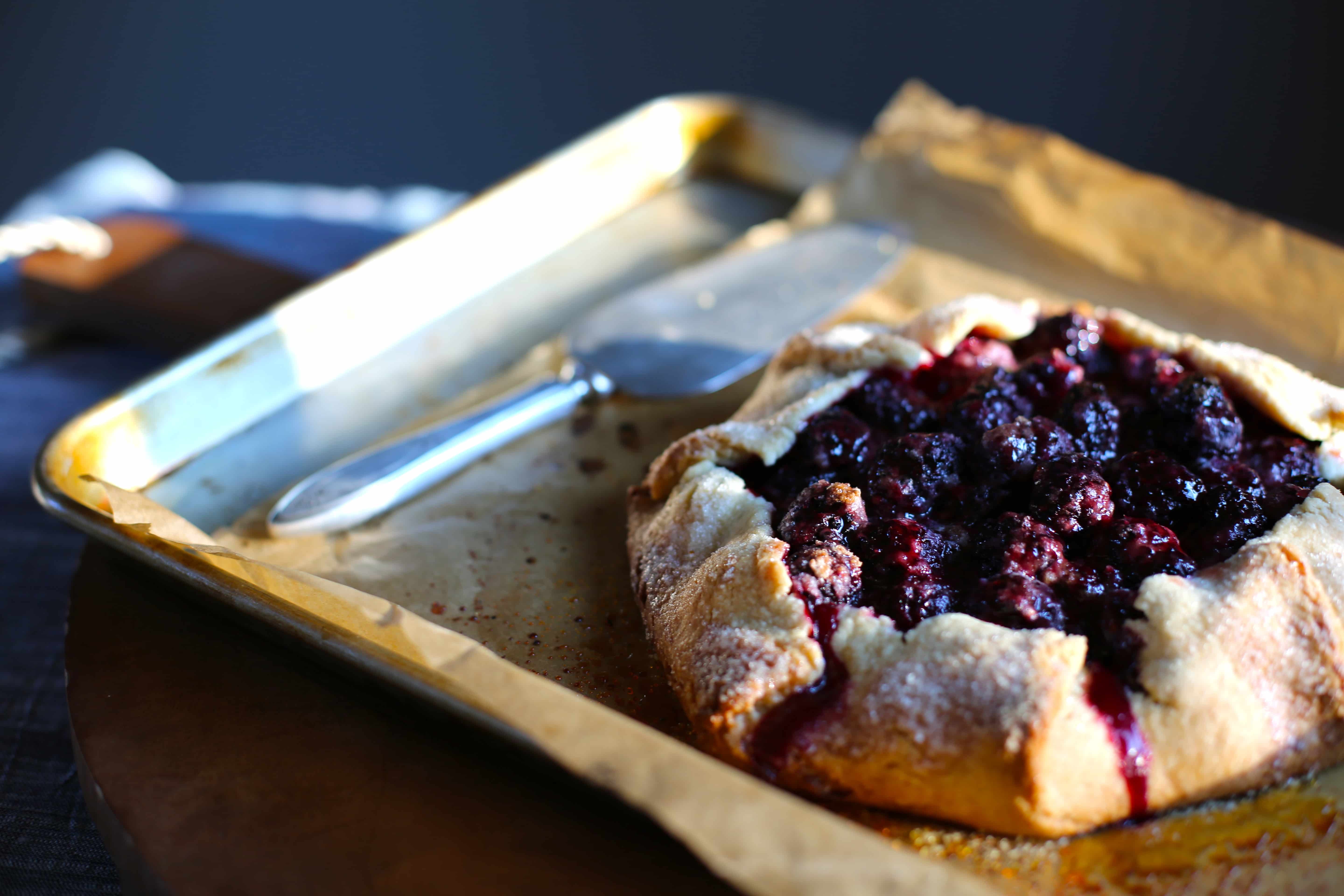  a blackberry galette/tart on a baking sheet with a serving utinsil 