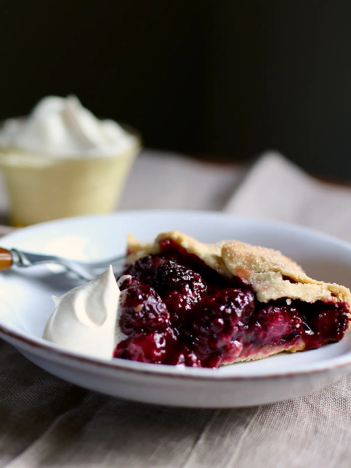 a piece of berry pie with whipped cream on white plate.