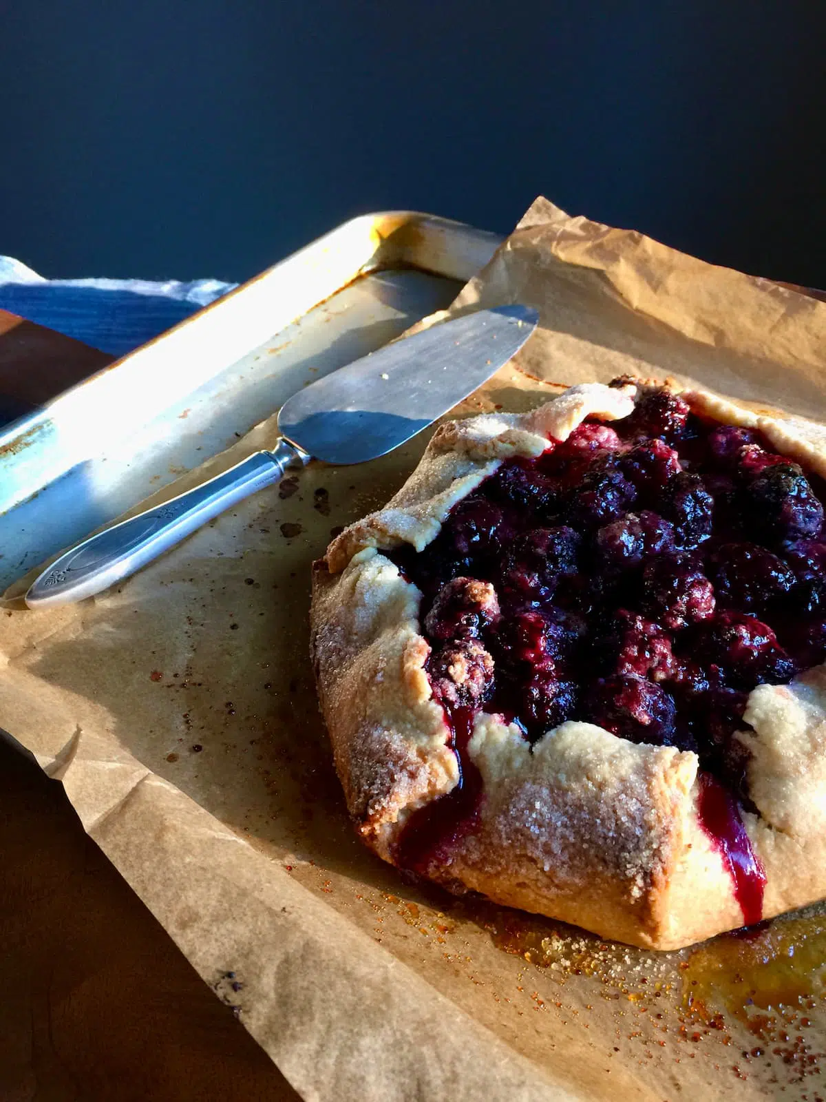 a galette with berries on a large baking sheet with a serving utinsil next to it.