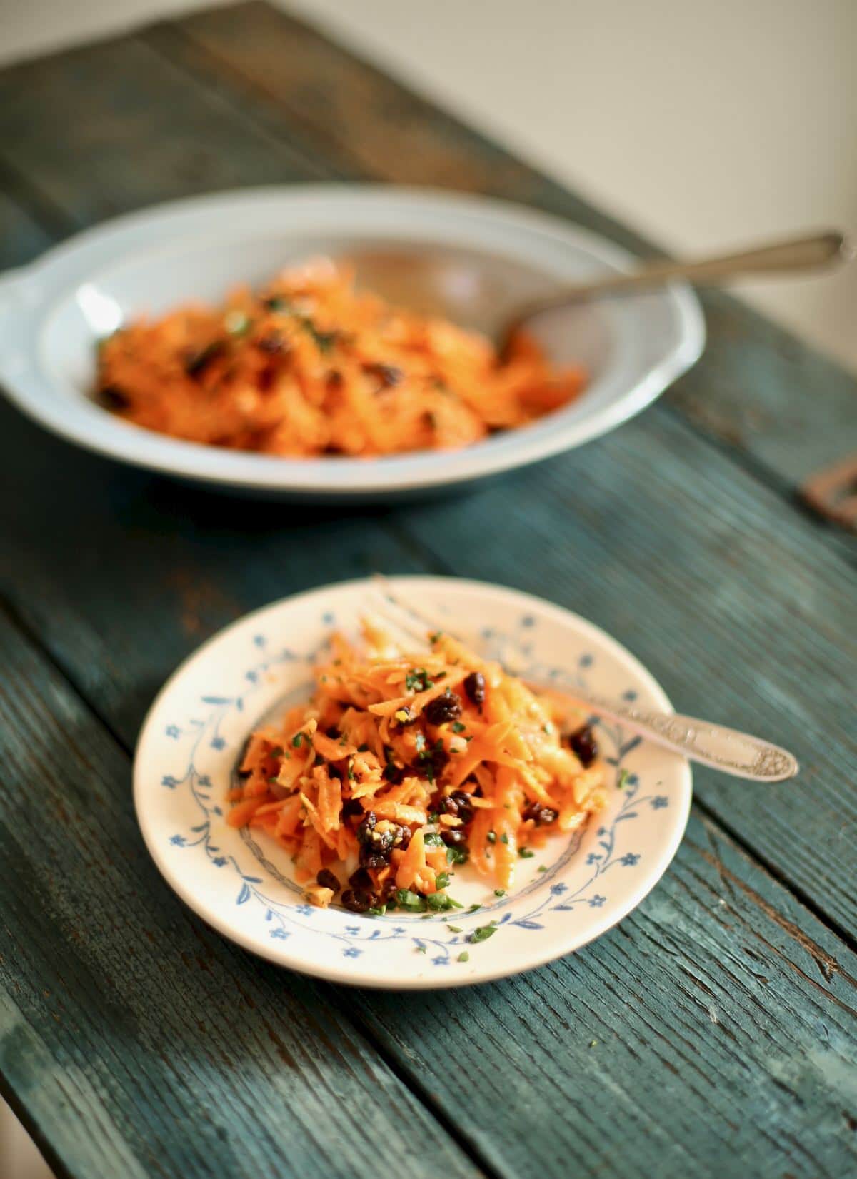 carrot salad on a plate with a fork and a bowl of it in background