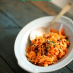 carrot salad on a table with a spoon in a blue bowl