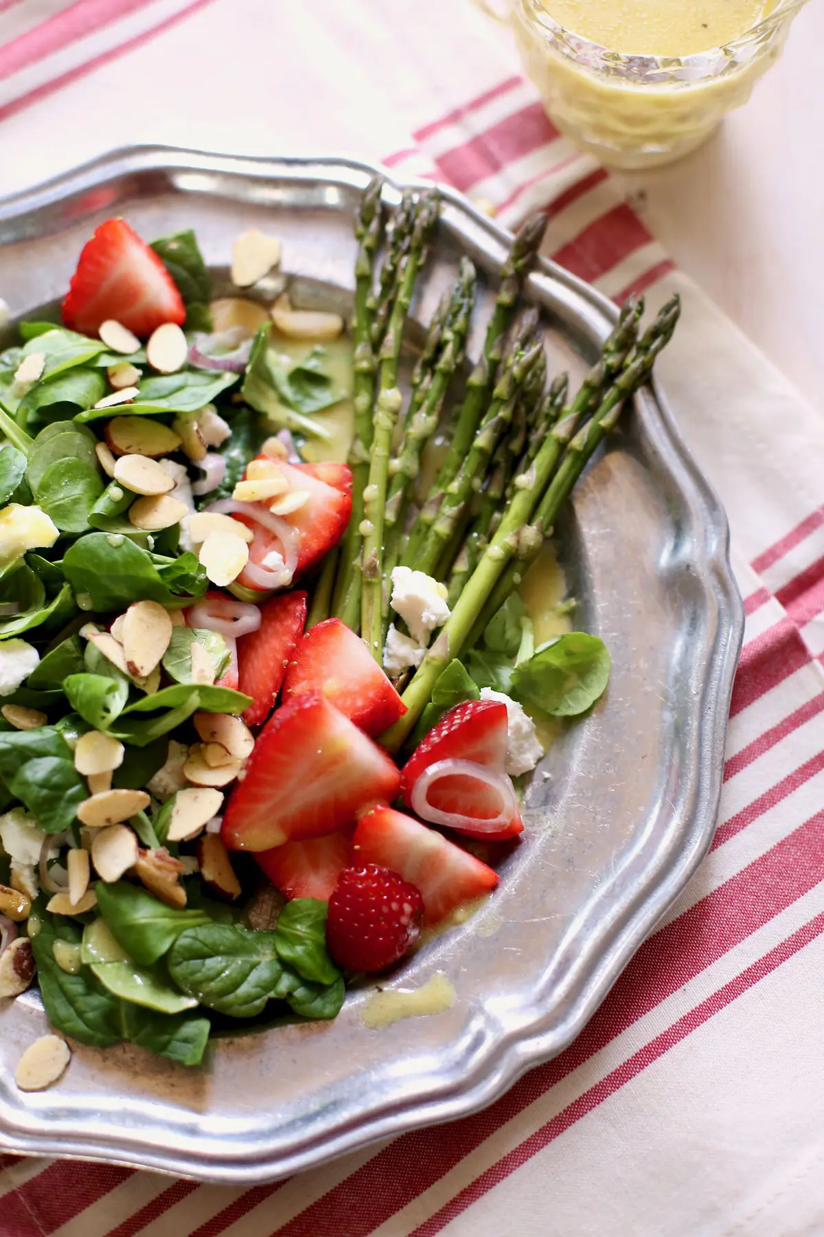 green salad on a silver plate with dressing in the background on a striped tablecloth. 