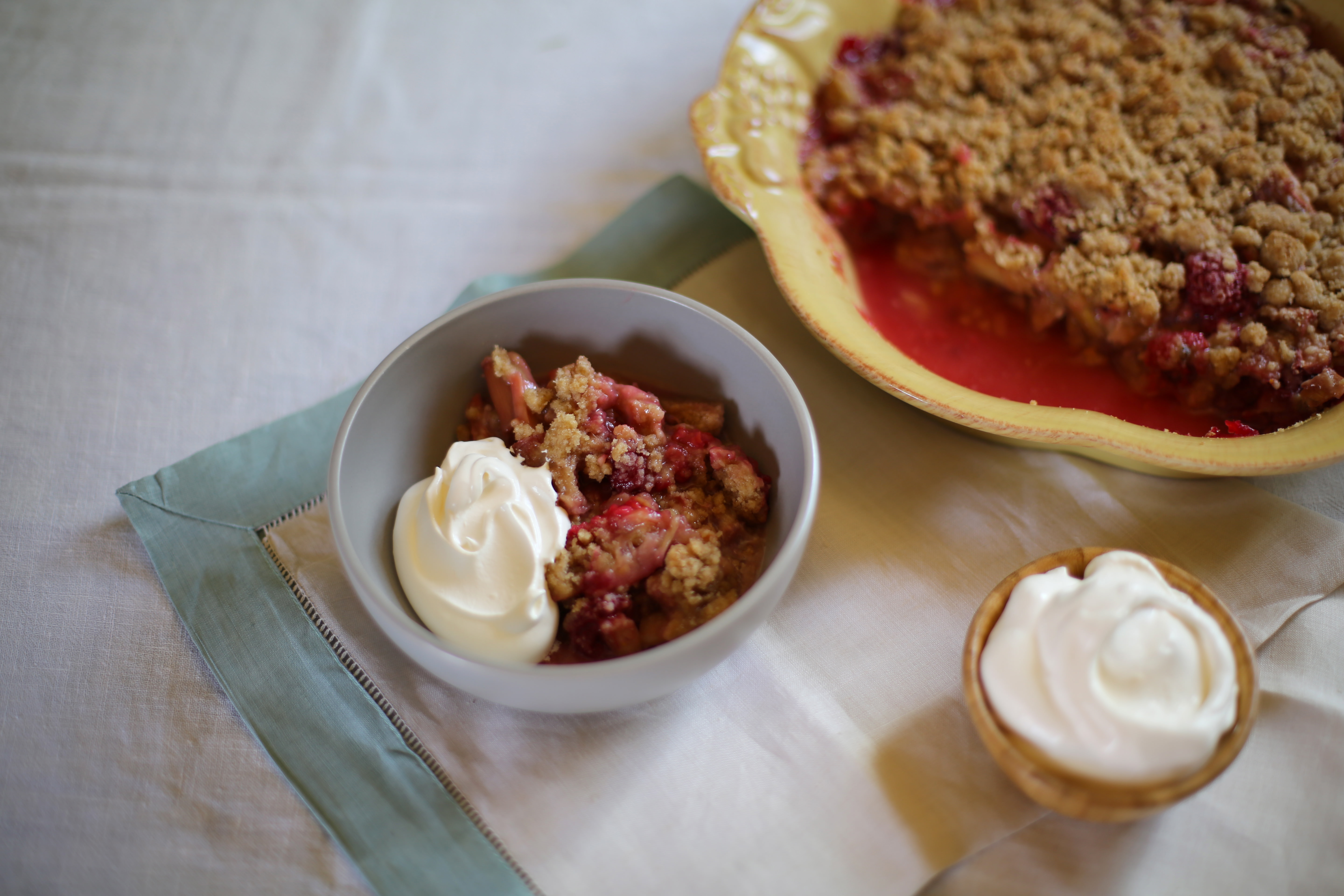 a baking dish and a serving of a fruit crisp with whipped cream on a table. 