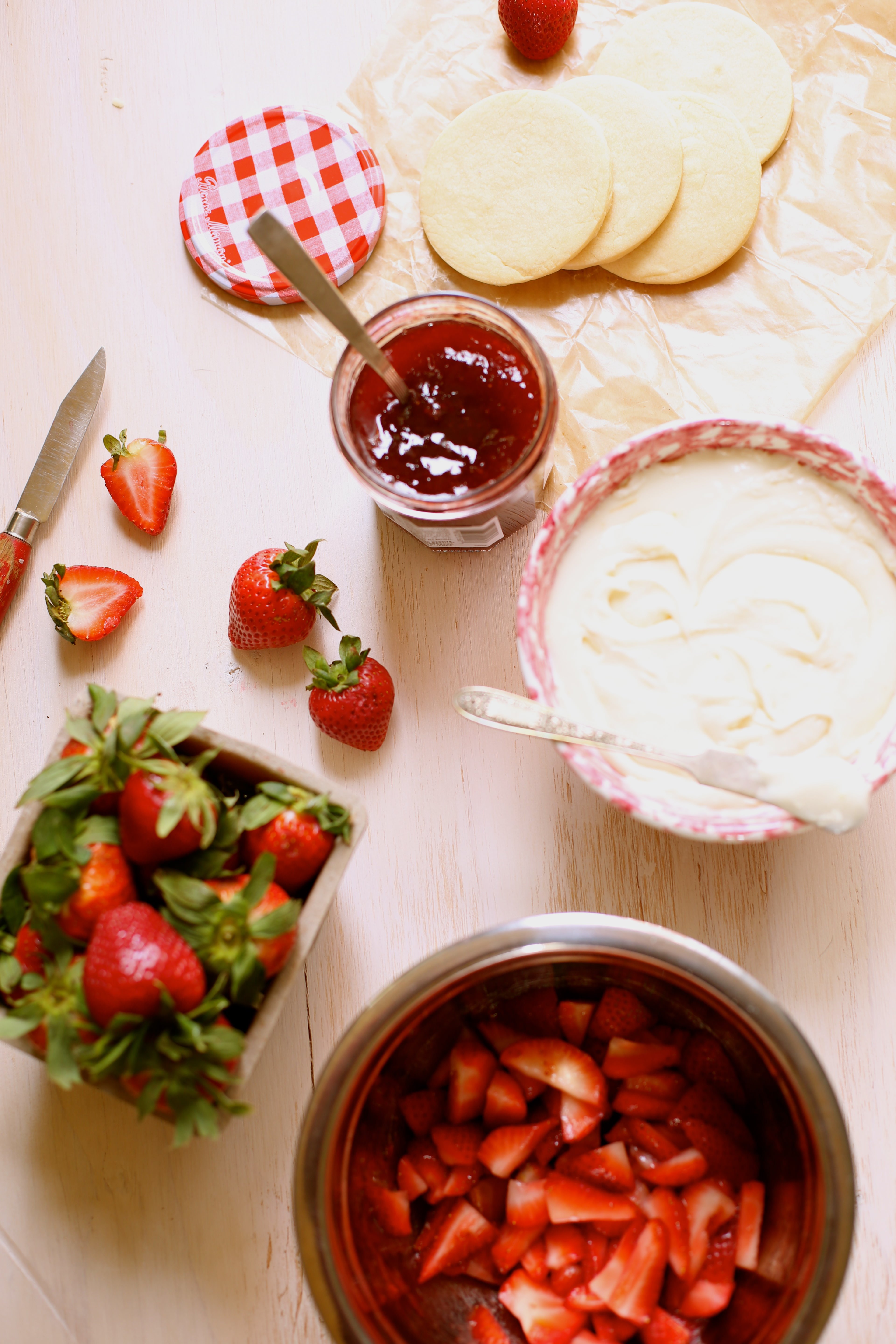 a bowl of strawberries, cream and jam on a table with a knife  