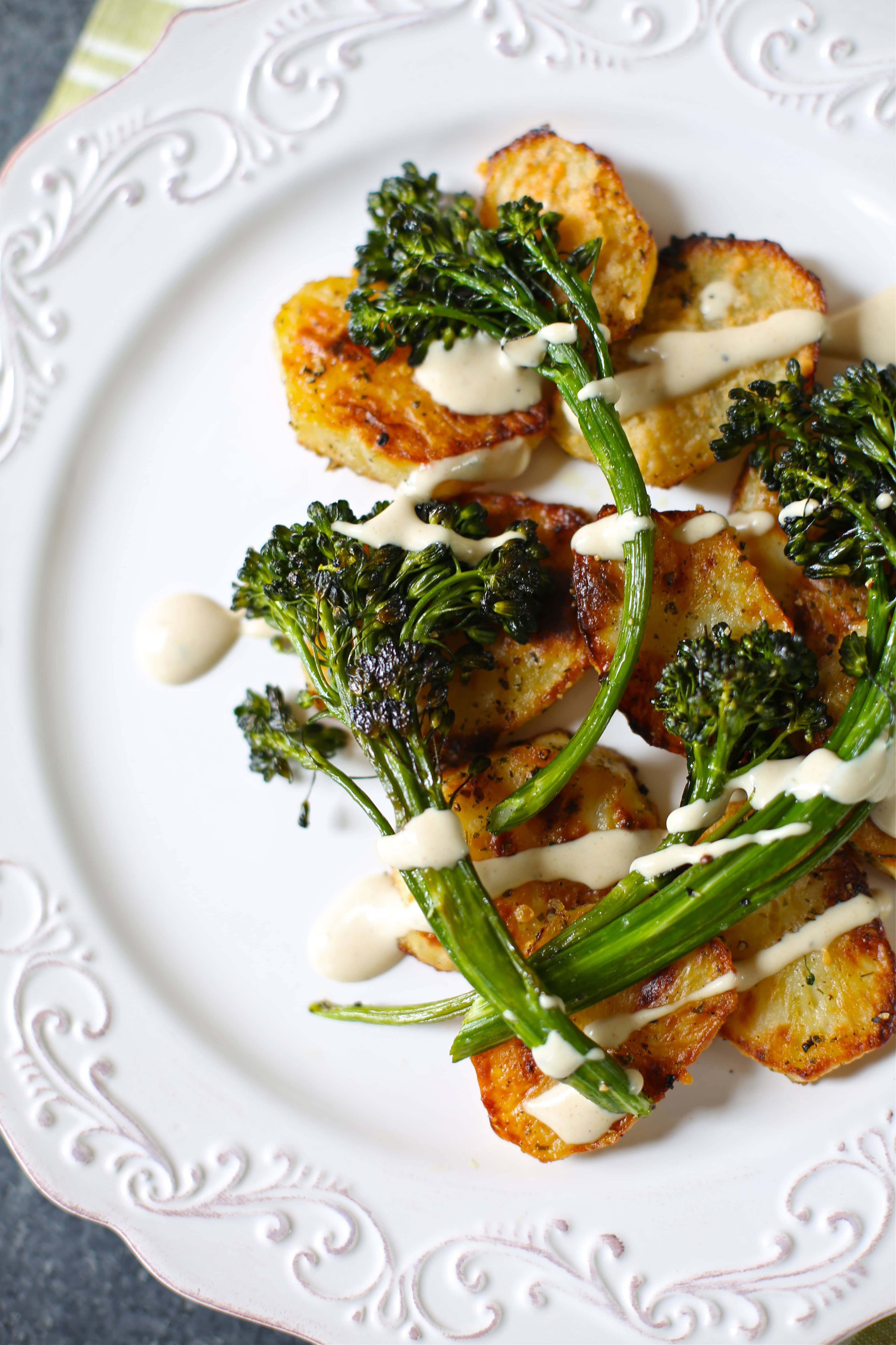 a white platter with roasted potatoes and broccolini with a sauce on top. 