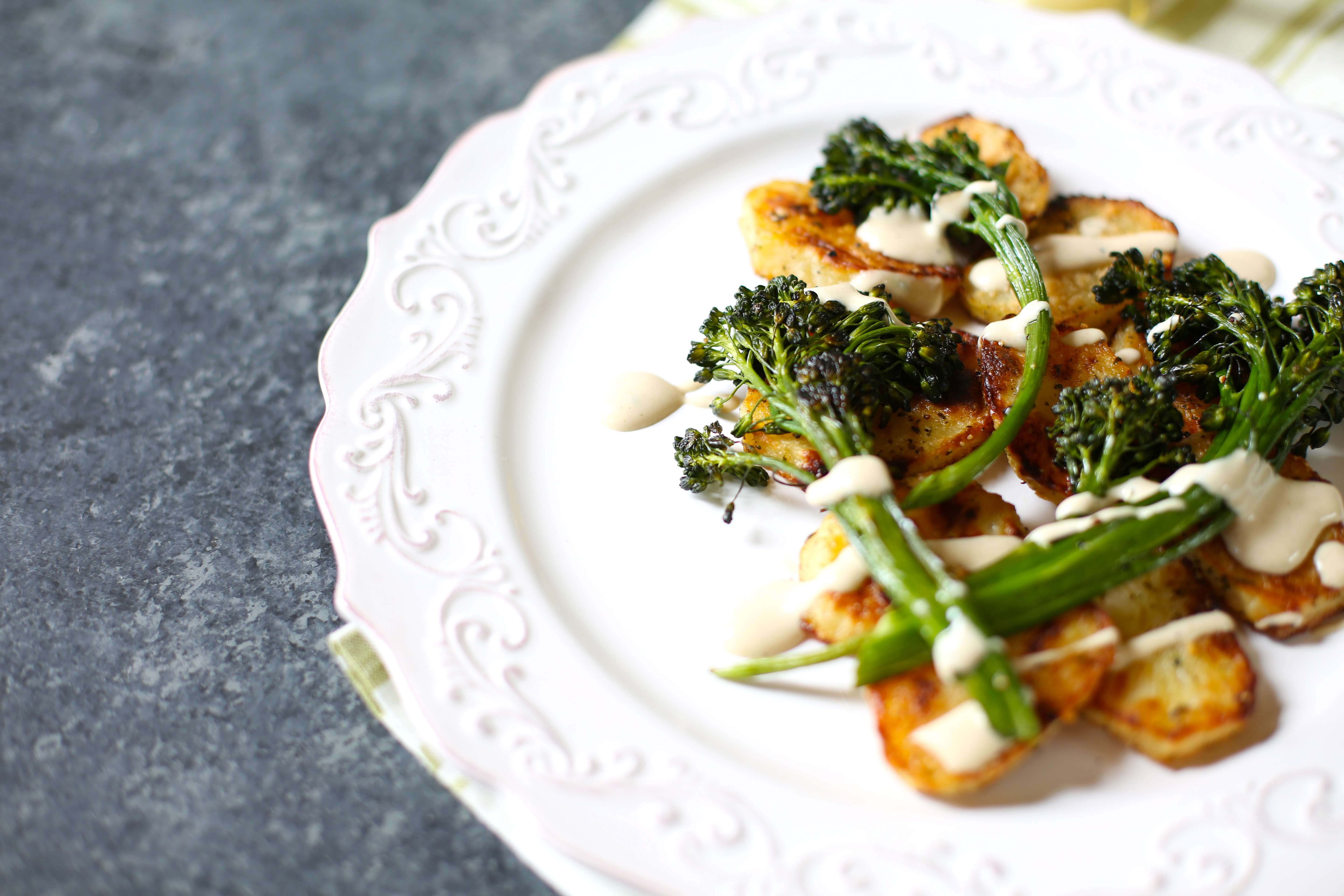 potatoes with roasted broccolini with  a sauce on top on a white platter on a gray table. 
