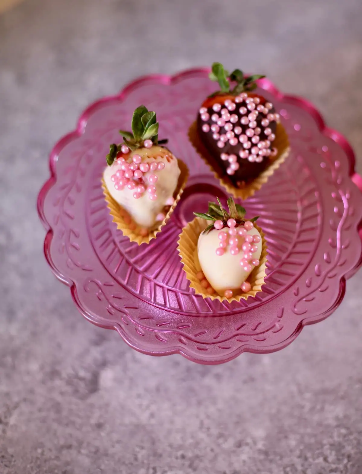 three strawberries dipped in chocolate and poink sprinkles on a pink plate 