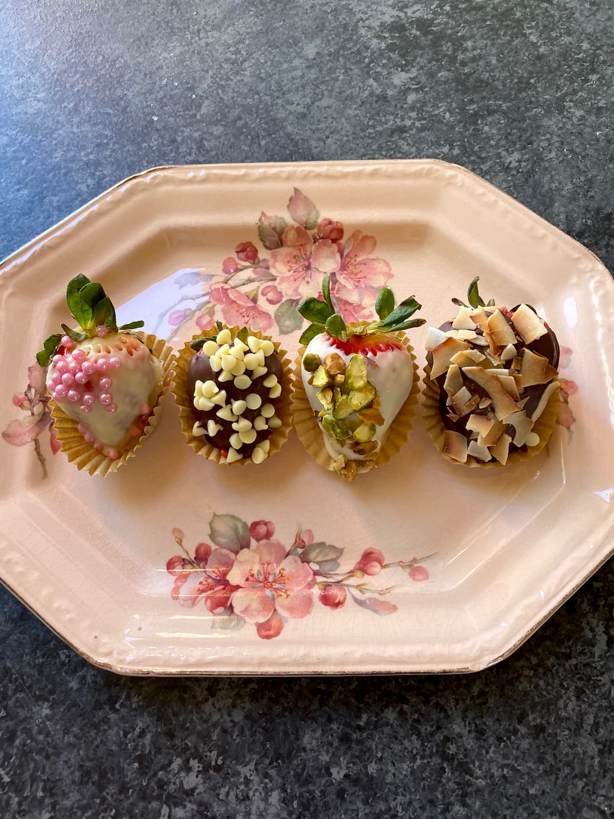four chocolate dipped strawberries on a flowered pink plate 