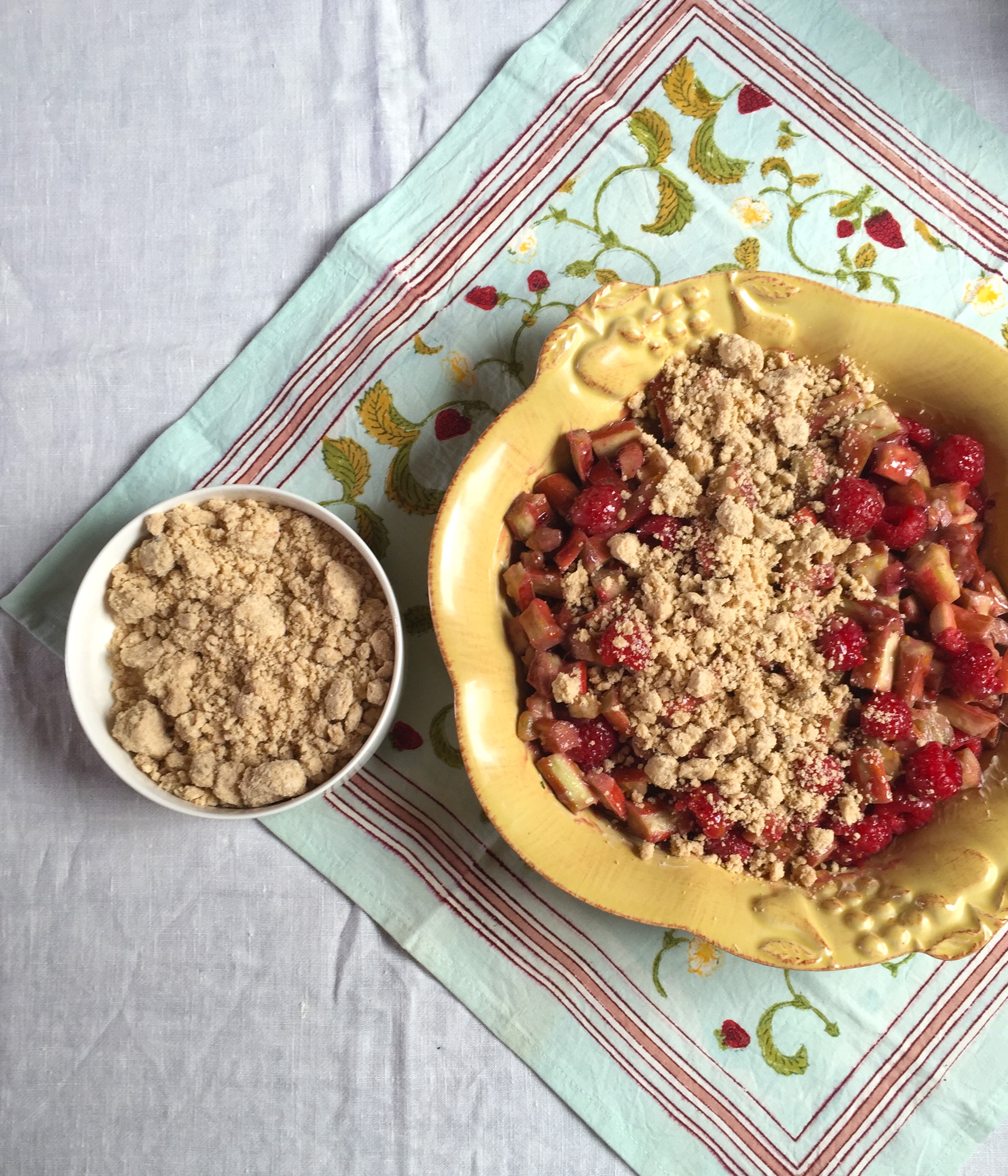 a yellow baking dish of Raspberry Rhubarb Crisp and a small white bowl next to it of just the topping for the recipe 