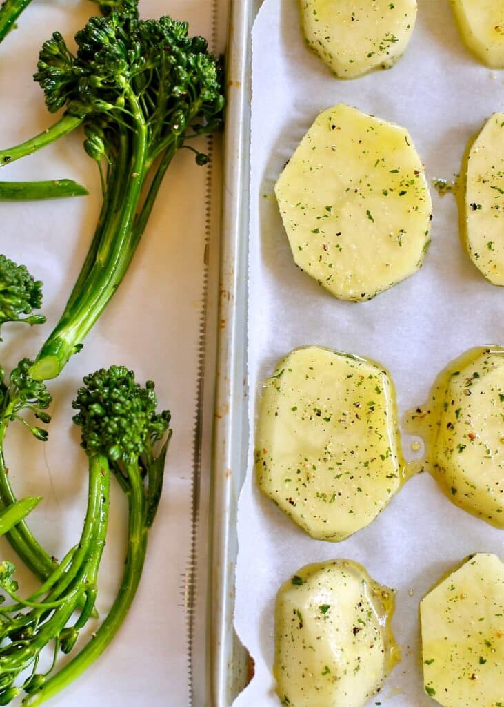 a photo of raw potatoes and broccolini on a baking sheet.