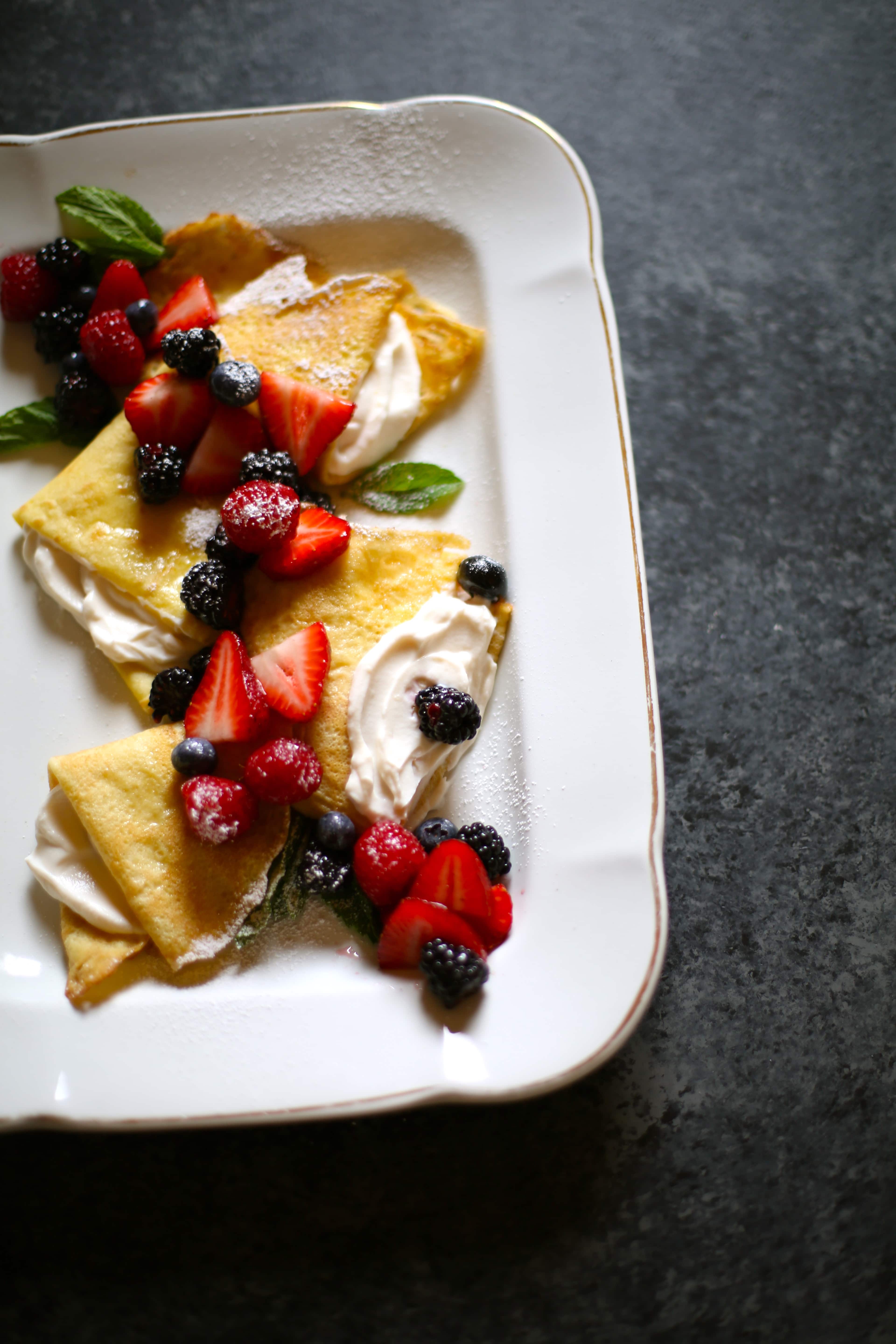 A large white platter of crepes with fresh fruit on top.  