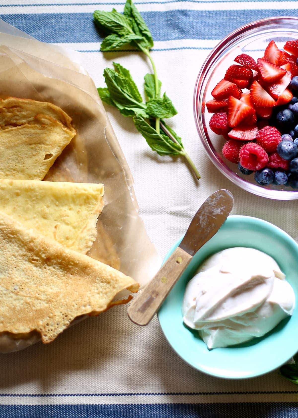 a table with crepes, berries and whipped cream in a bowl.