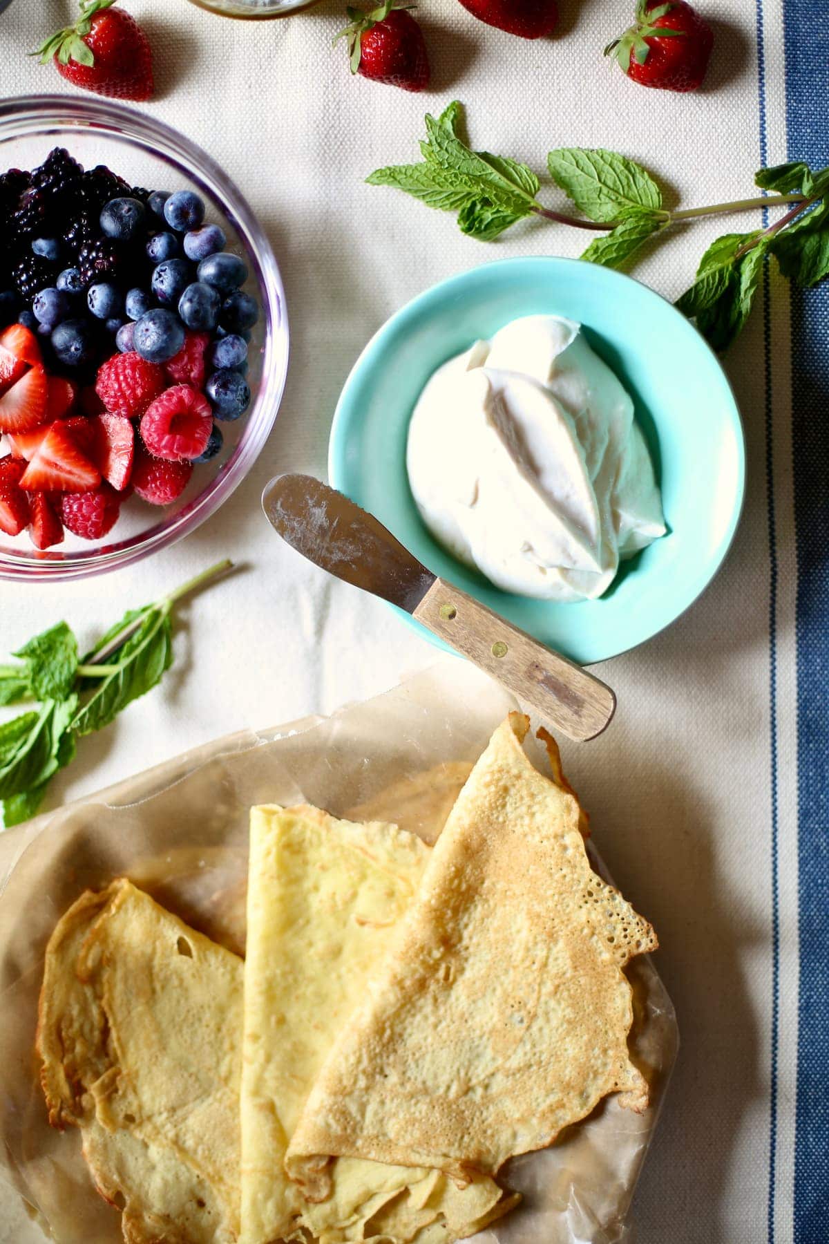 a table with whipped cream, crepes and berries.