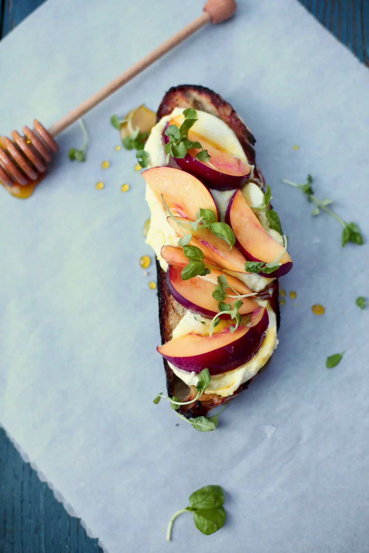 a slice of toast with nectarines and honey and basil on a table with a honey dipper on the side. 