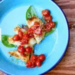 chicken with cherry tomatoes on top in a blue skillet