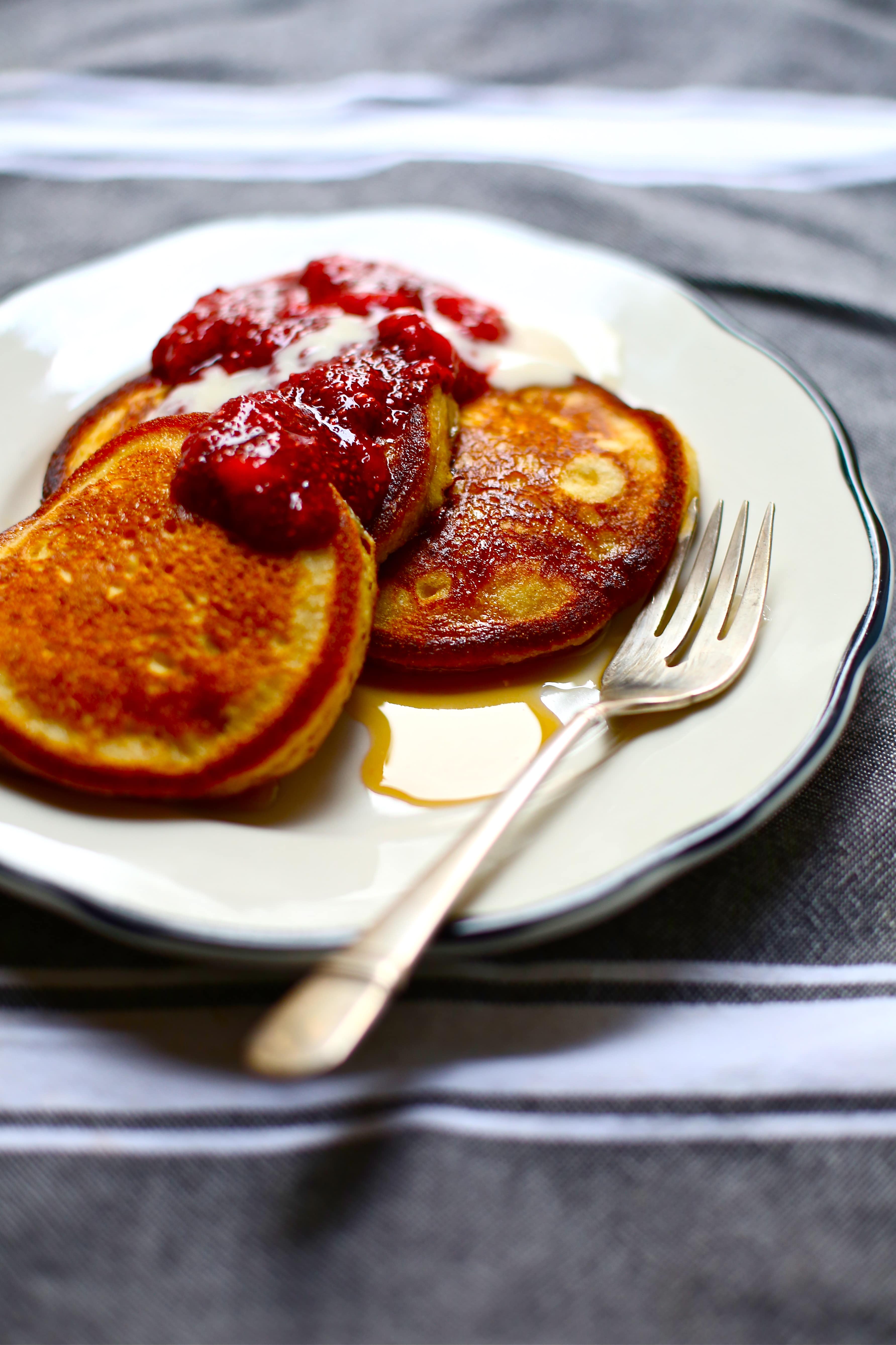  Pancakes with Strawberry Jam on a white plate with a silver fork on a gray background. 