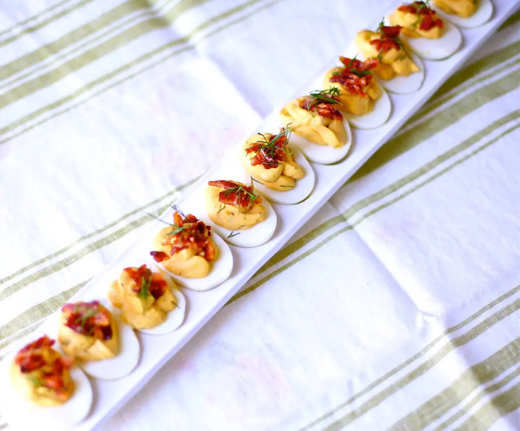 Deviled Eggs with Candied Bacon and Fresh Dill on a striped linen surface 