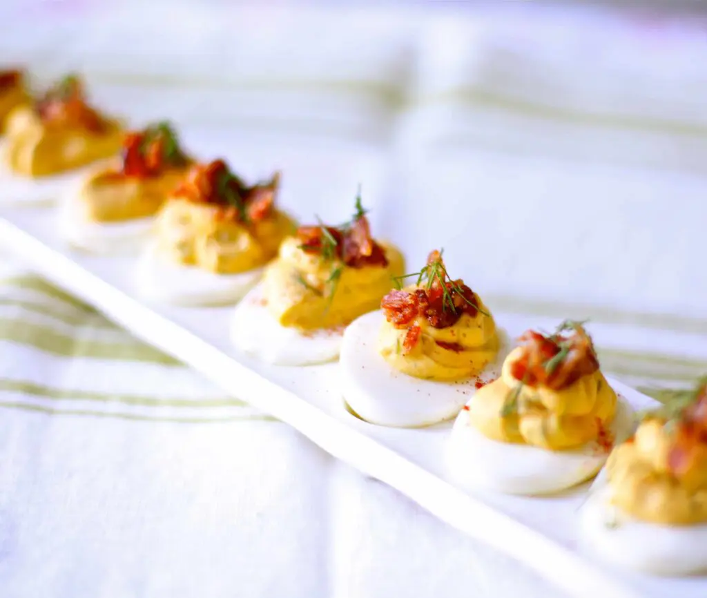 Deviled Eggs with Candied Bacon and Fresh Dill on a white tray 