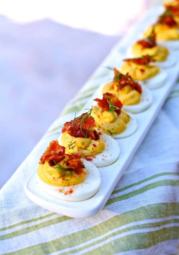 Deviled Eggs with Candied Bacon and Fresh Dill on a white plate and striped tablecloth 