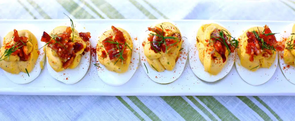 Deviled Eggs with Candied Bacon and Fresh Dill on a white tray on striped linen
