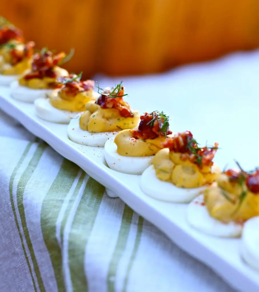 Deviled Eggs with Candied Bacon and Fresh Dill on ledge with striped linen 