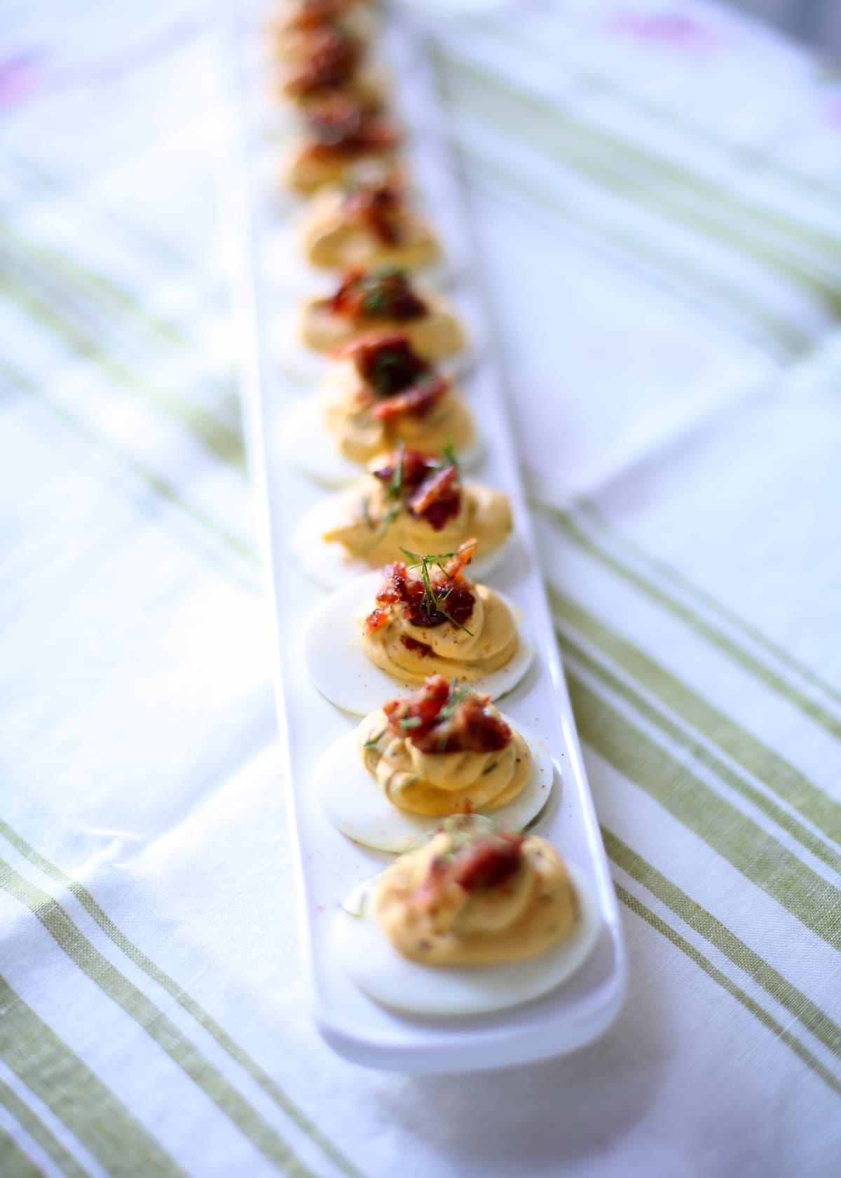 a vertical photo of deviled eggs on a table with striped tablecloth.