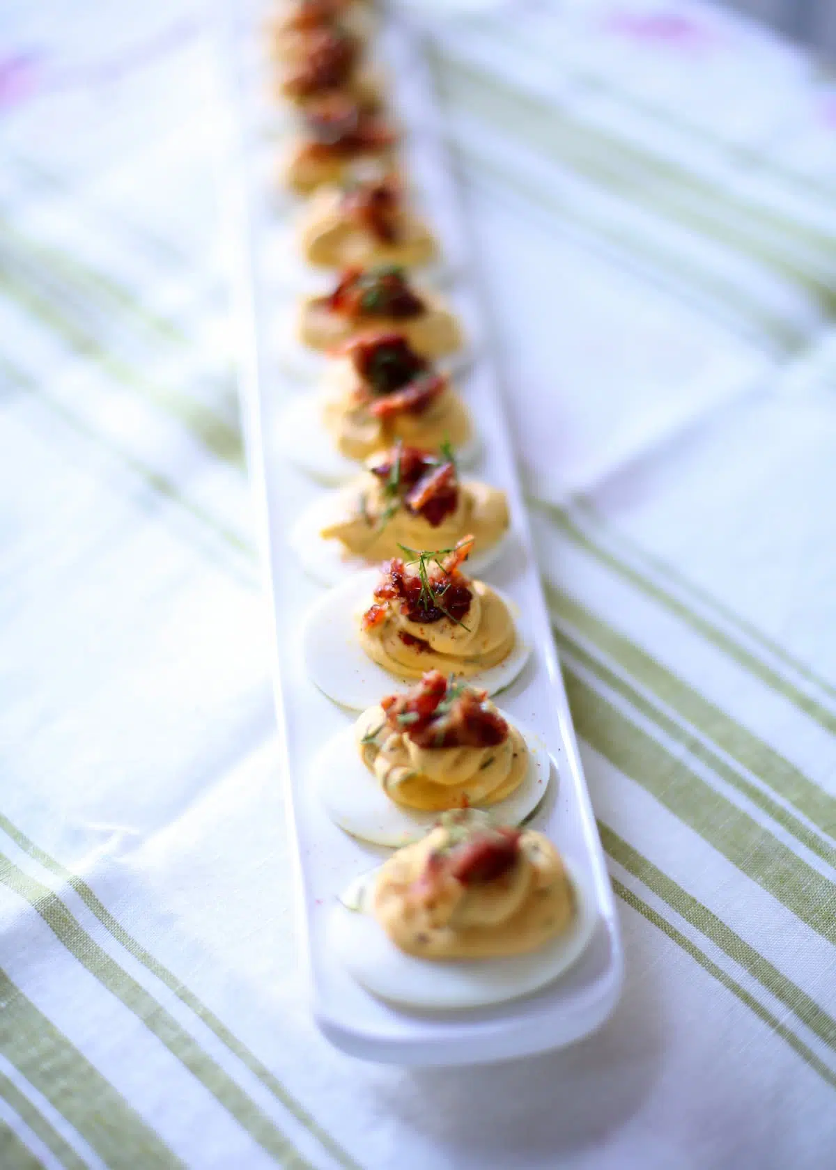 a vertical photo of deviled eggs on a table with striped tablecloth.