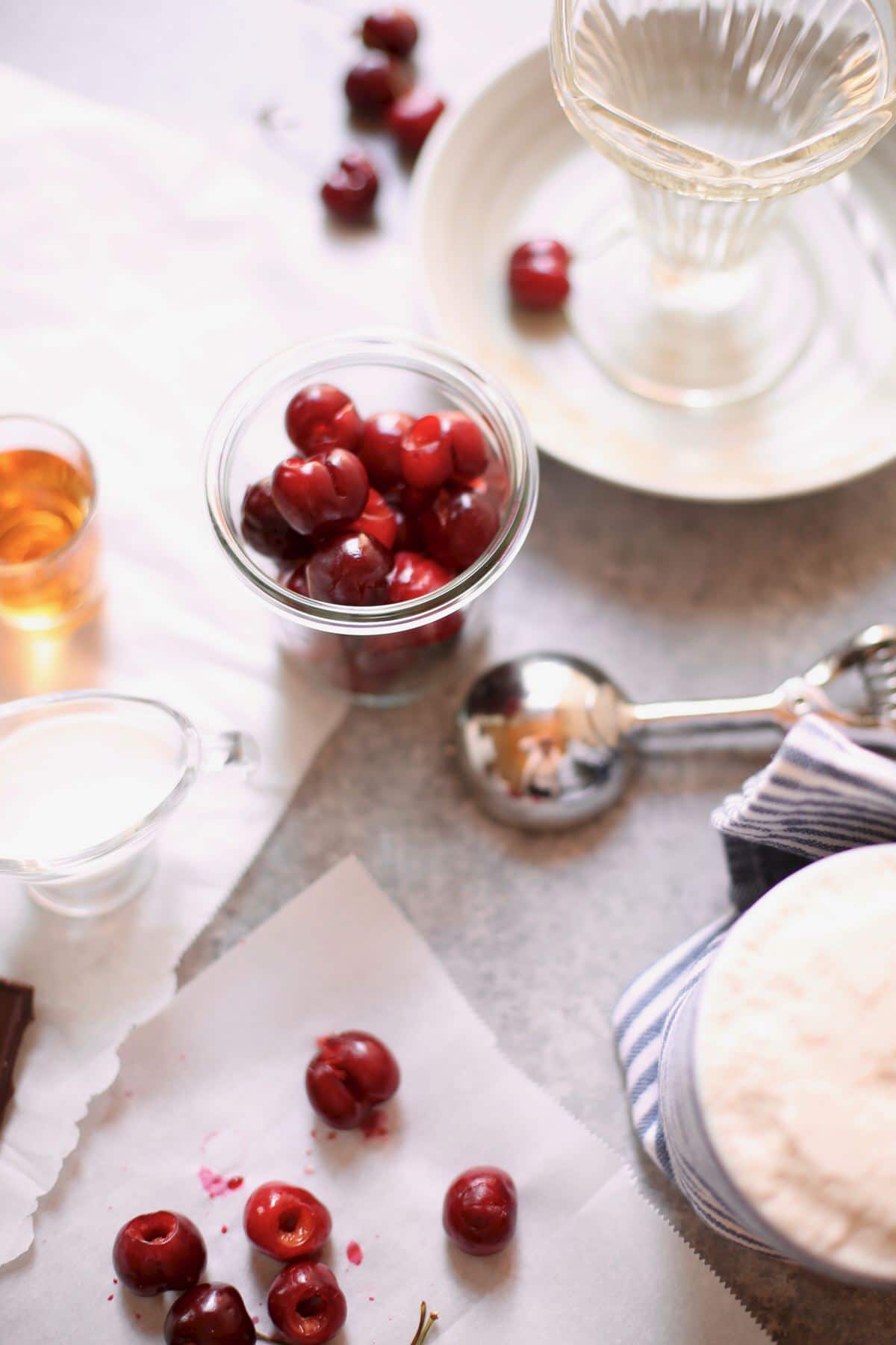 cherries and an ice cream scoop and cream on a gray table 