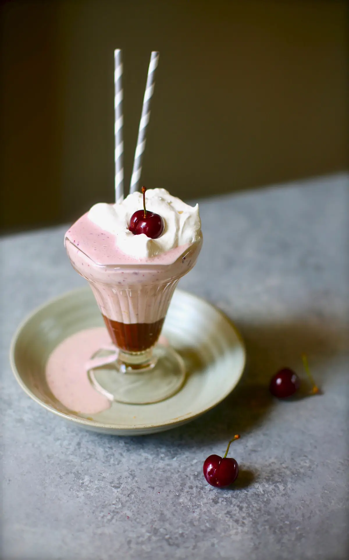 a cherry milkshake on a gray plate and table with two straws