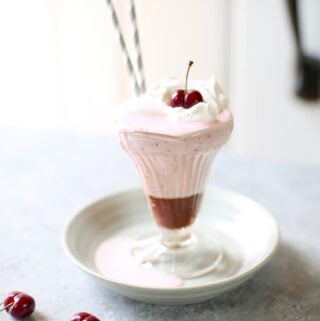 a cherry milkshake on a gray plate and table with cherries next to it