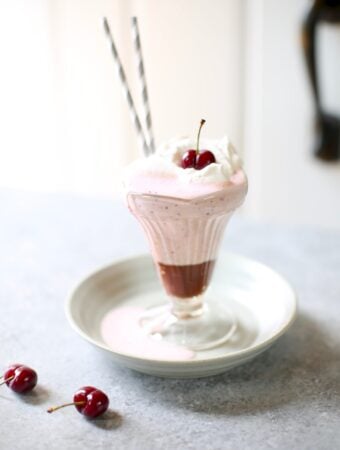 a cherry milkshake on a gray plate and table with cherries next to it