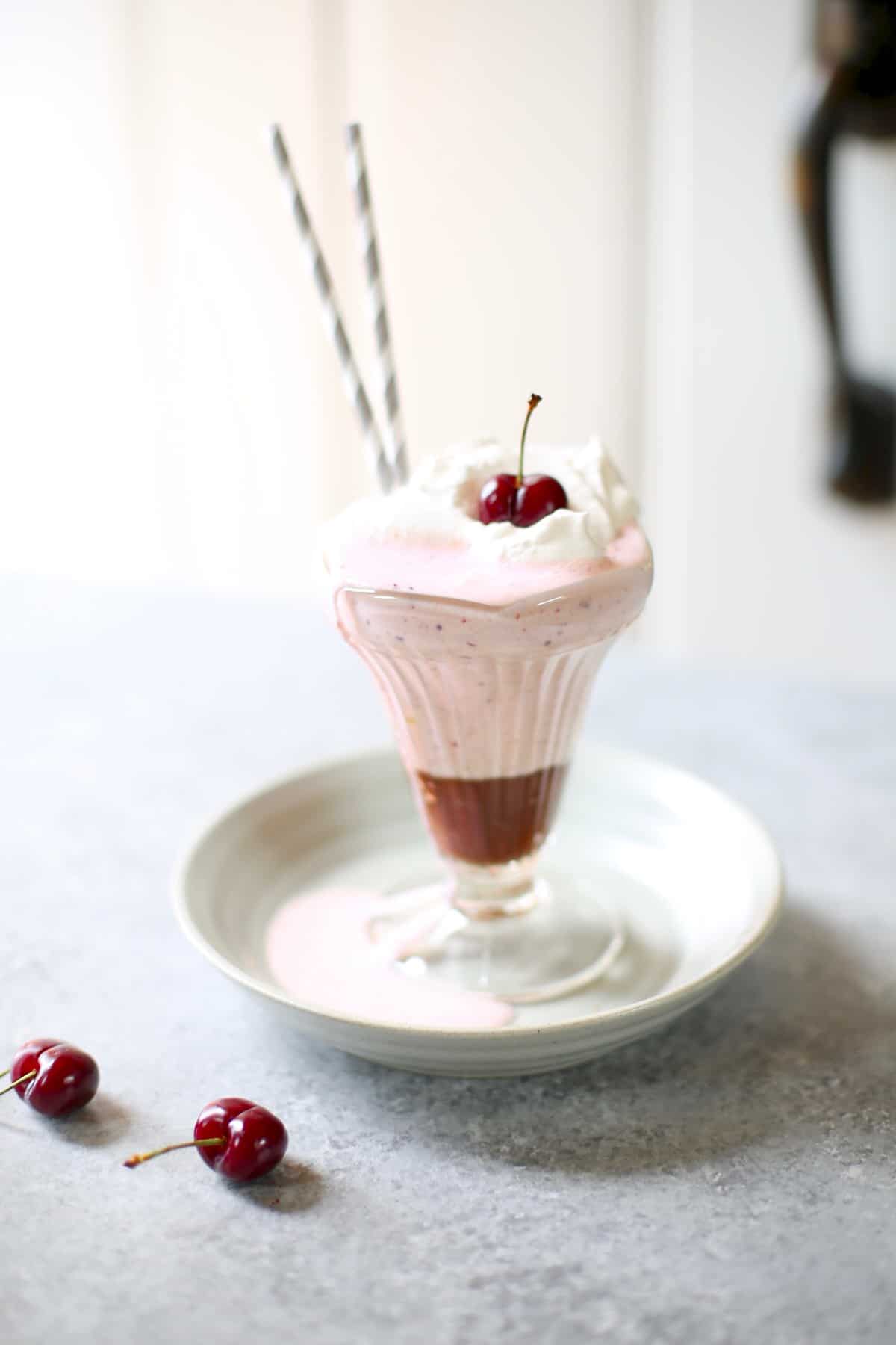 a cherry milkshake on a gray plate and table with cherries next to it 