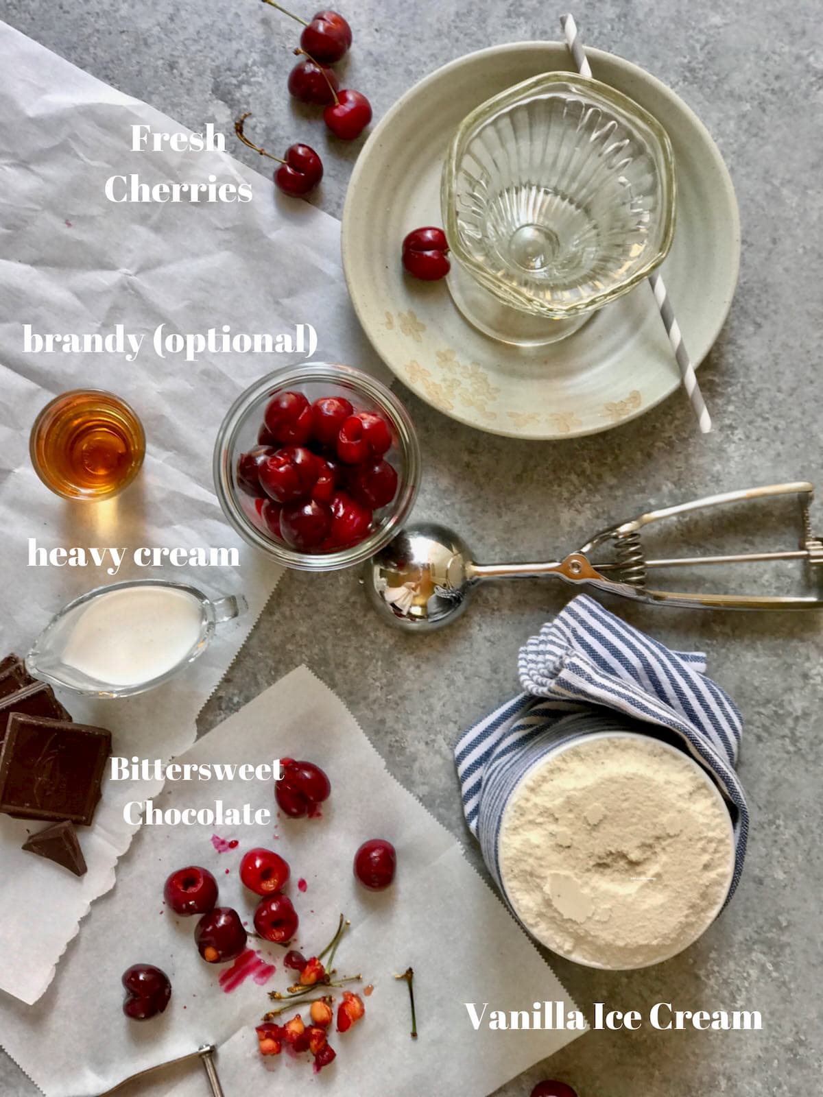 cherries, a glass, vanilla ice cream, booze and an ice cream scoop on a gray table 