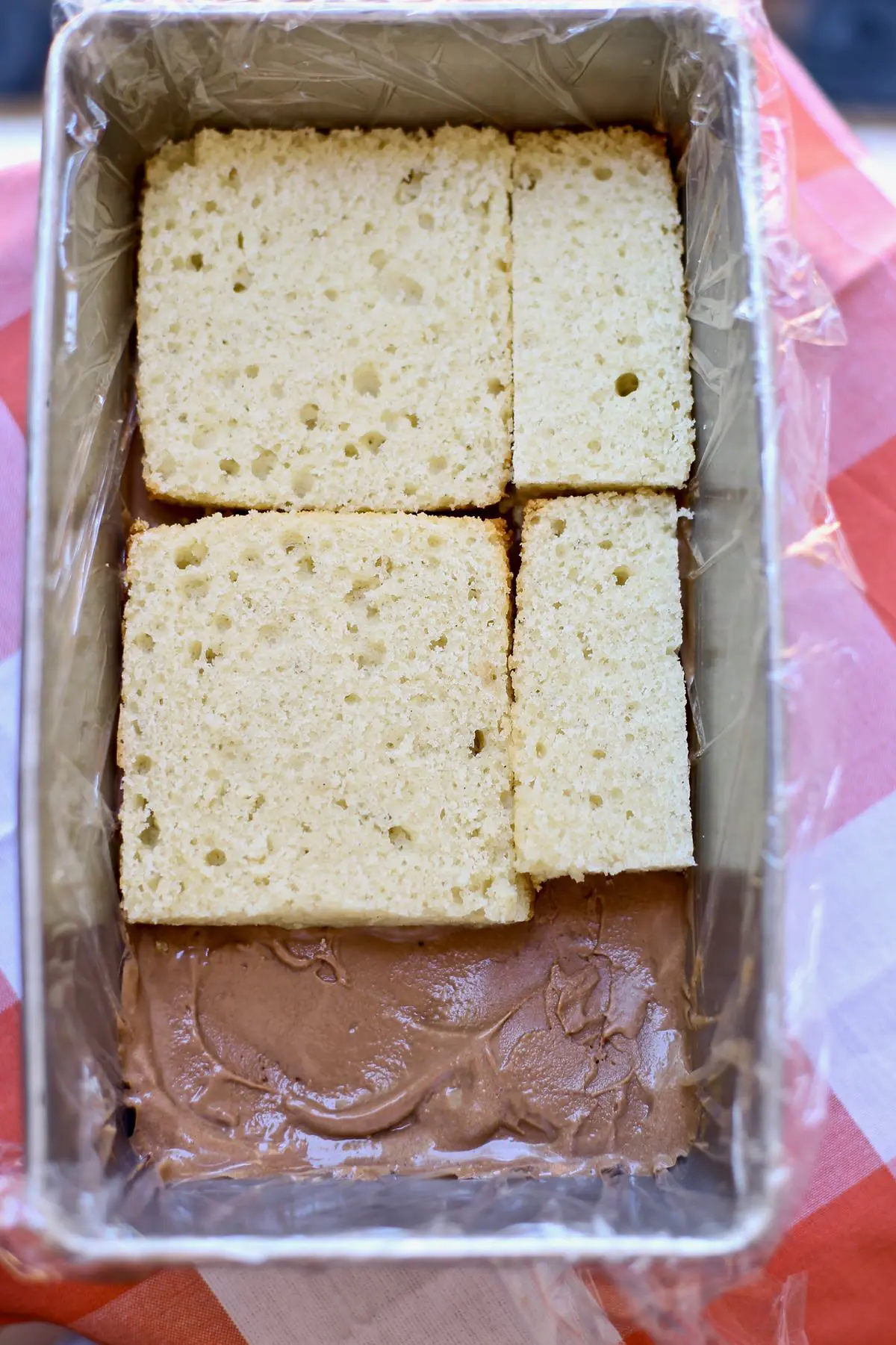 cake is layered on chocolate ice cream in a loaf pan on red tablecloth