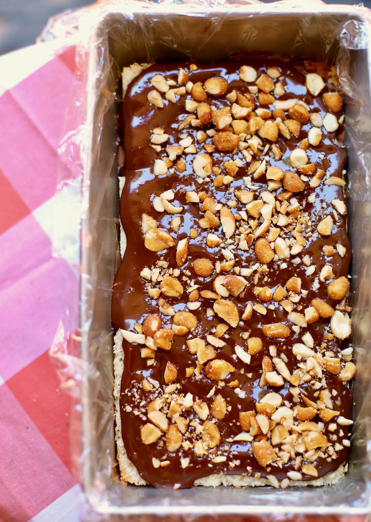 ice cream cake with ganache and chopped peanuts on a read and white tablecloth