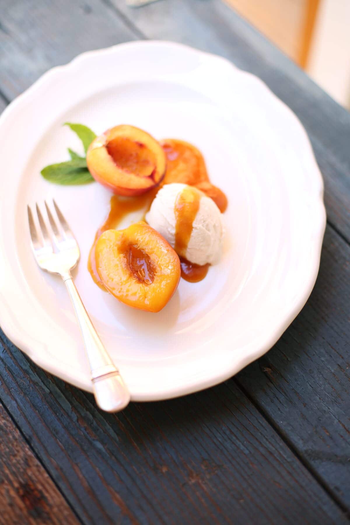 nectarines with caramel sauce and ice cream on a white plate with silver fork
