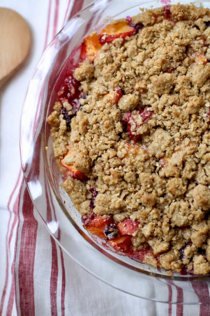 fruit crisp out of the oven in a plate on a striped tablecloth