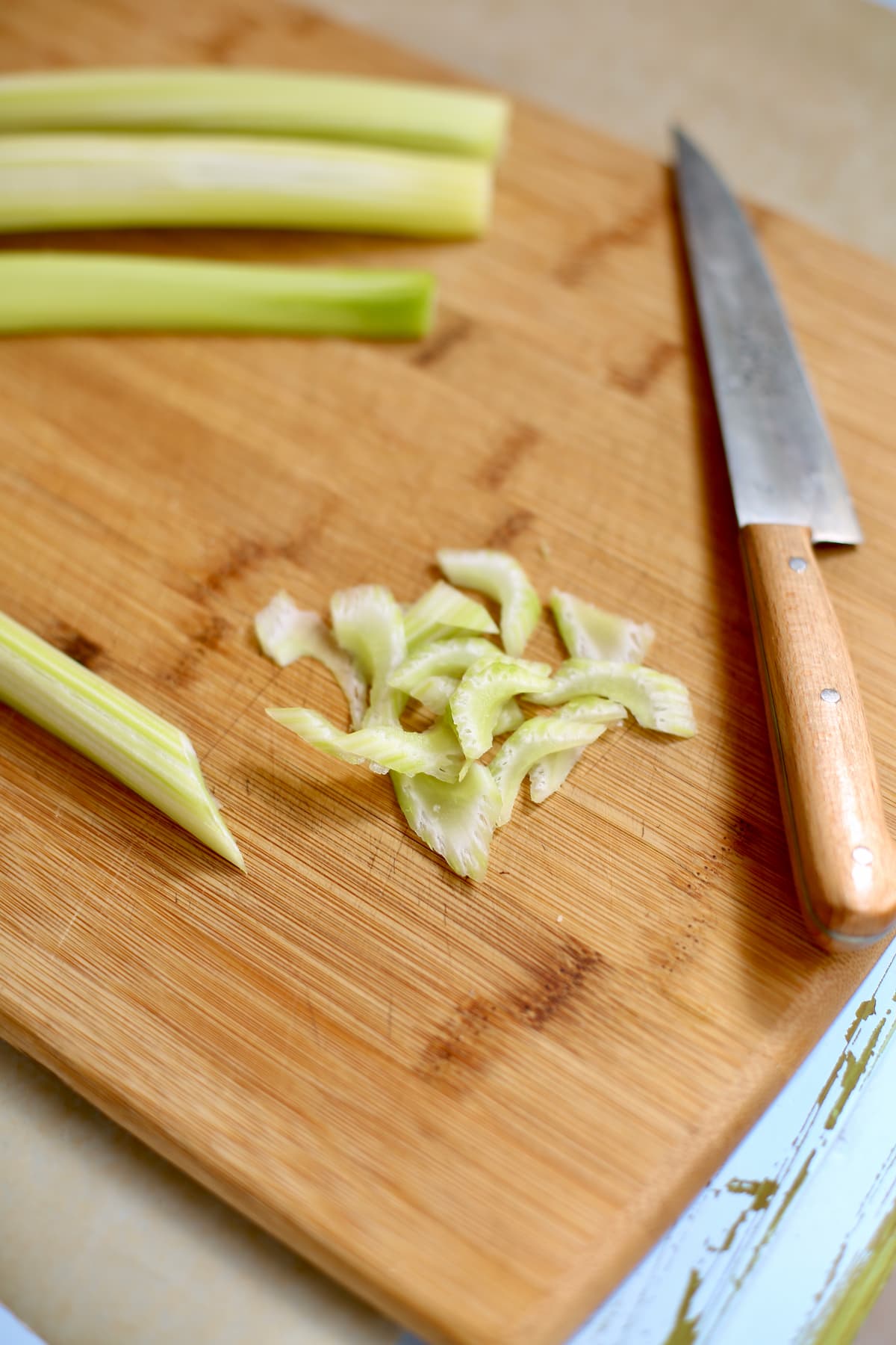 a cutting board with celery being sliced with a wooden knife.