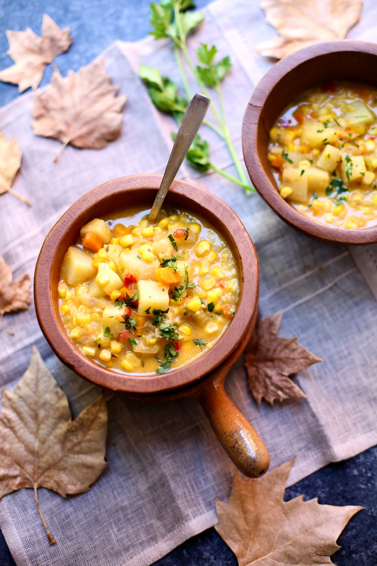 two bowls of corn soup on a table with leaves. 