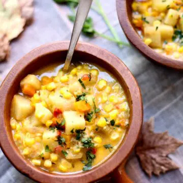 a bowl of corn chowder with a spoon in it on a table with fall leaves around it.
