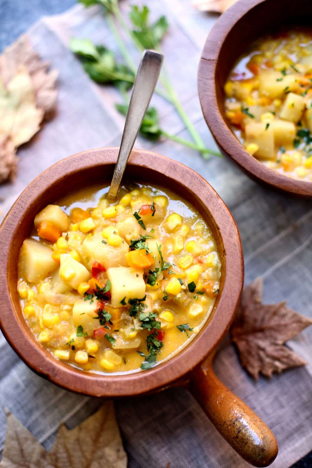 a bowl of corn chowder with a spoon in it on a table with fall leaves around it.