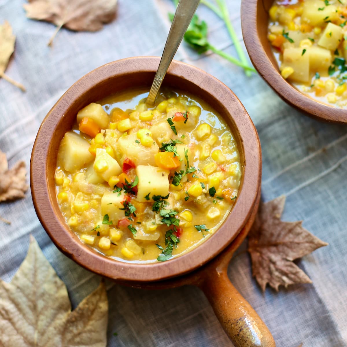 a bowl of corn chowder with a spoon coming out of it on a table with leaves.