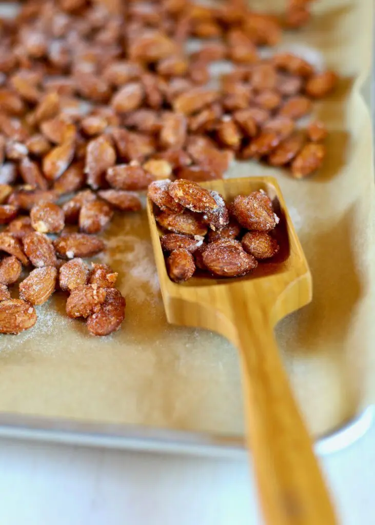 almonds that have been roasted on a baking sheet with a wooden spoon
